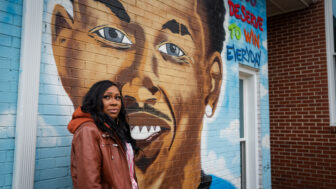 Woman standing before mural of her son who was shot