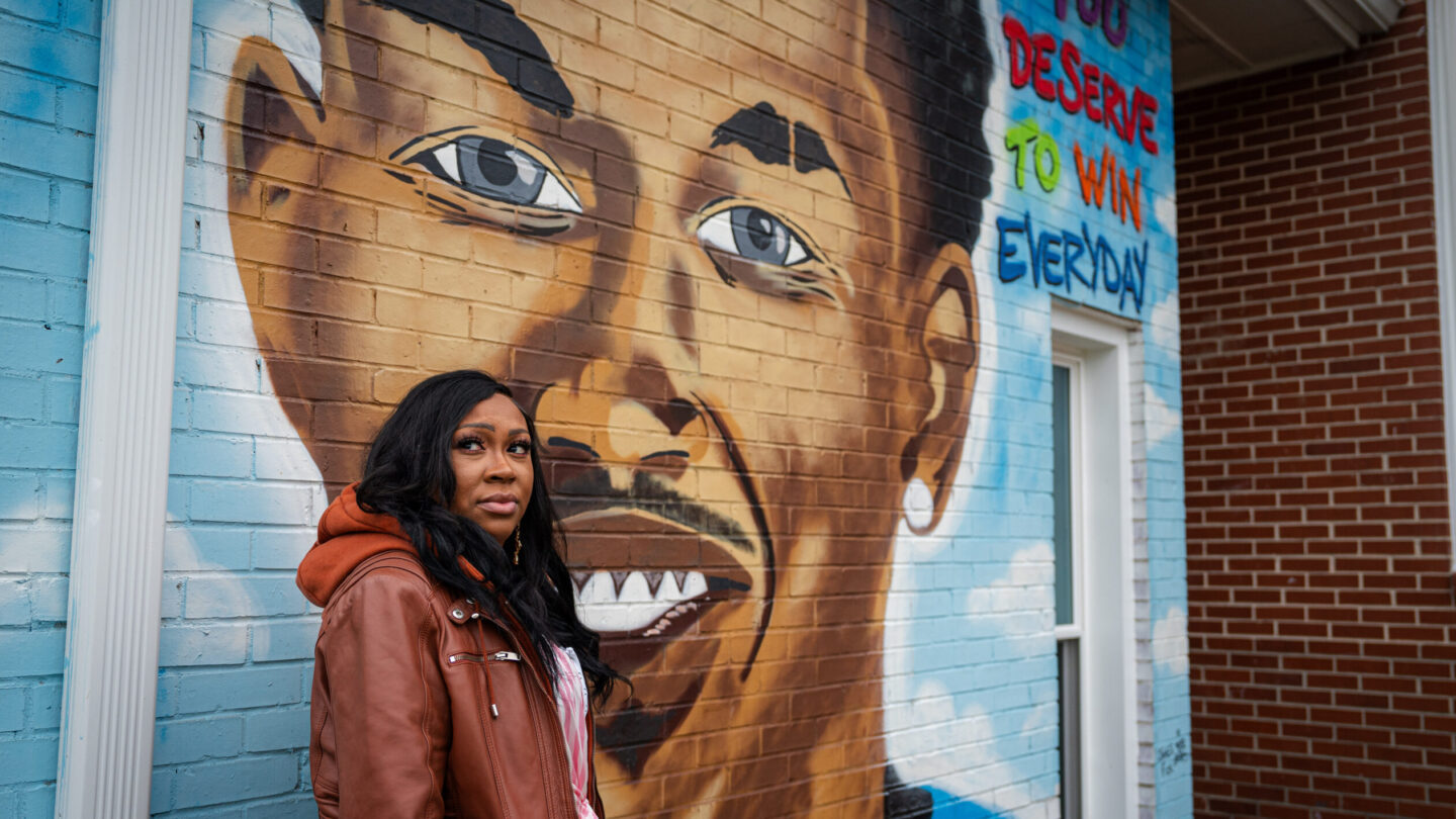 Woman standing before mural of her son who was shot