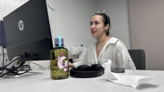 A woman in a white shirt looking up at a computer screen.