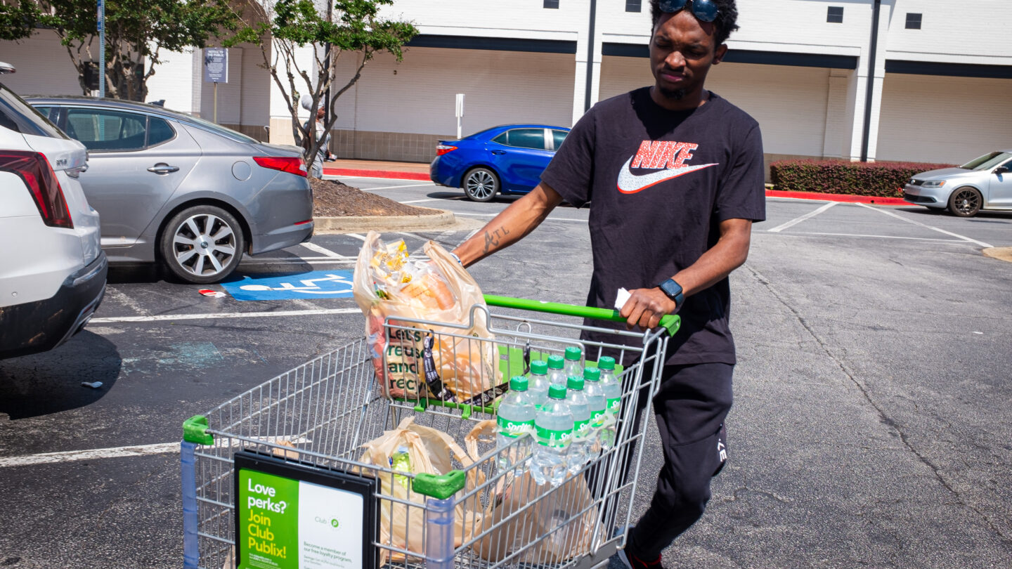 Young man pusing grocery cart on parking lot