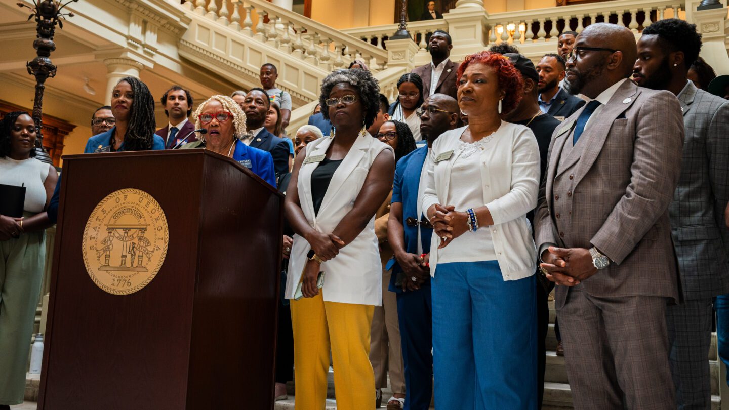 A group of teachers and advocates stand behind a podium at the Georgia State Capitol