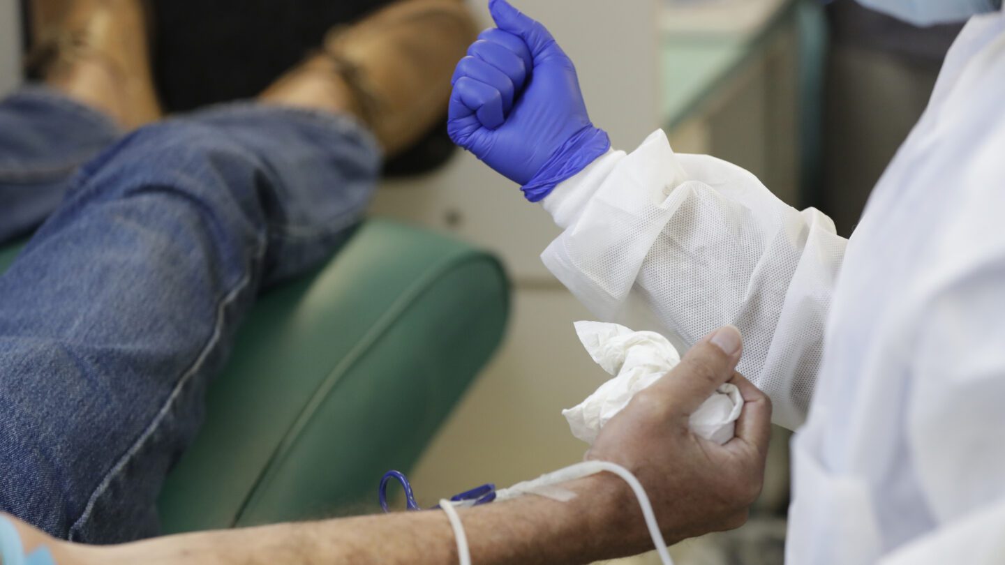 A phlebotomist makes a fist to instruct a patient to make a fist before he donates blood.