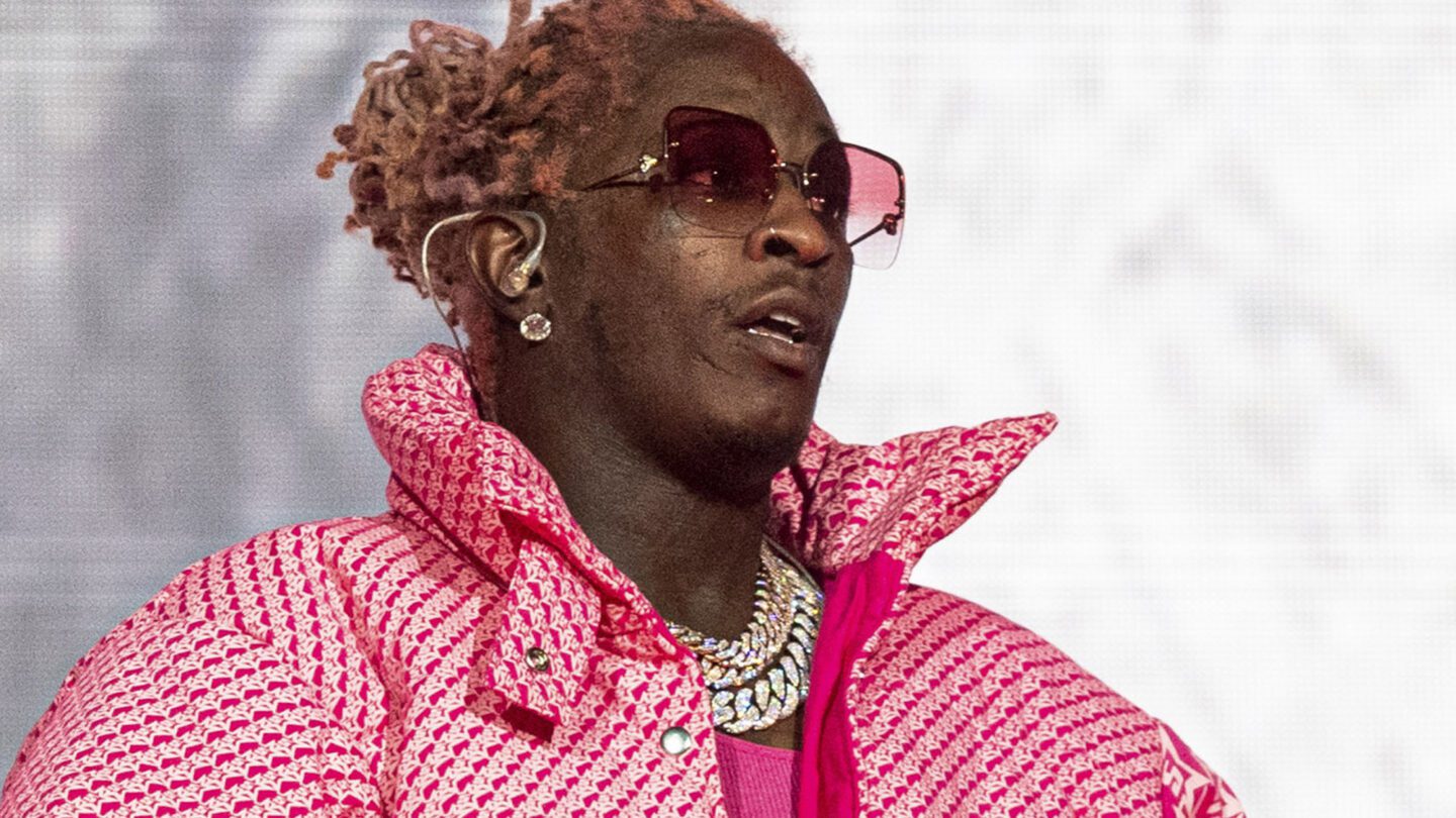 A closeup of Young Thug performing at Lollapalooza in 2021. He is wearing a pink coat and pink tinted glasses.