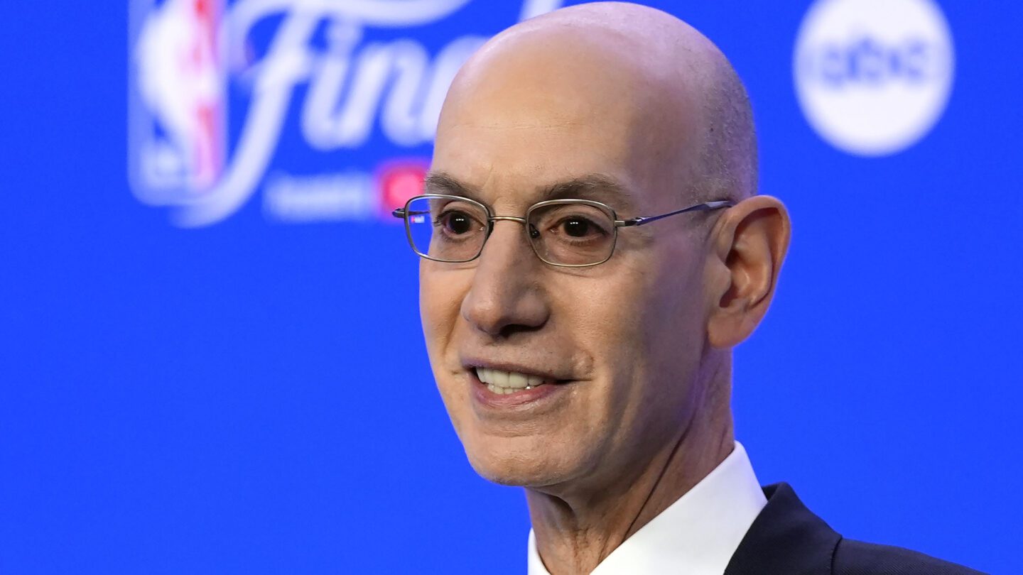 NBA Commissioner Adam Silver talks in front of a bright blue background.