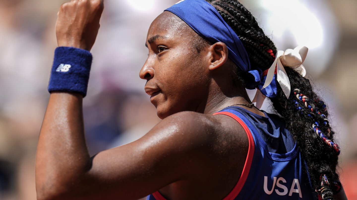 Coco Gauff, U.S. tennis Olympian, has a hand raised in the air while looking to the left.