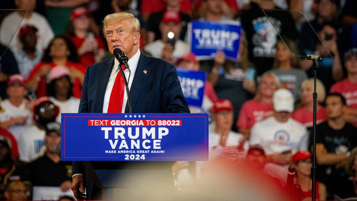 Donald Trump stands at a lectern with a crowd behind him at Atlanta rally.