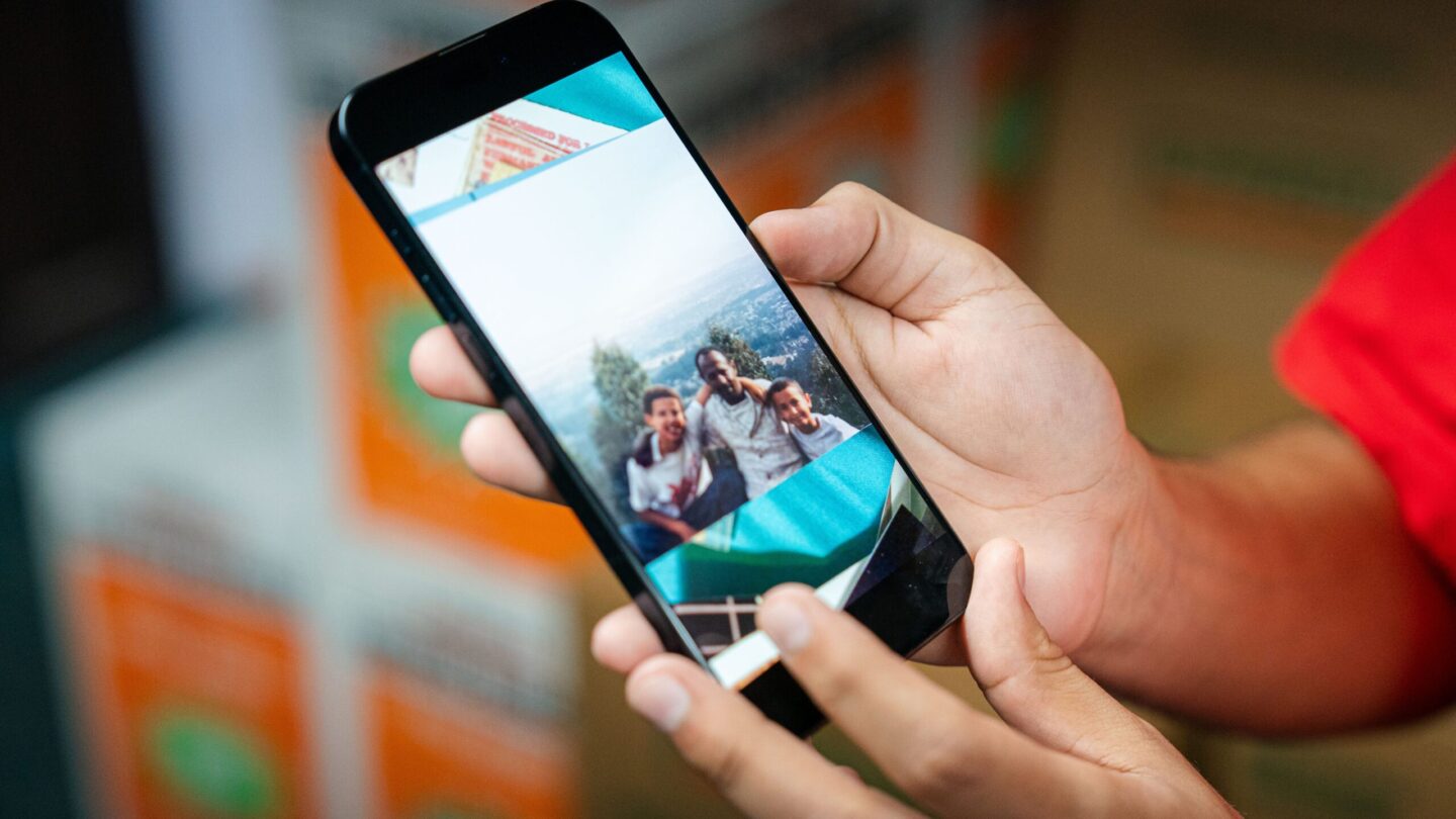 Adam Davis holds his phone, showing a photo of himself, his dad and his older brother posing on top of a mountain in Ethiopia.