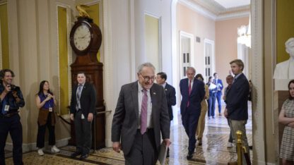 Chuck Schumer walks through the halls of the U.S. Capitol amid a few reporters and staffers.