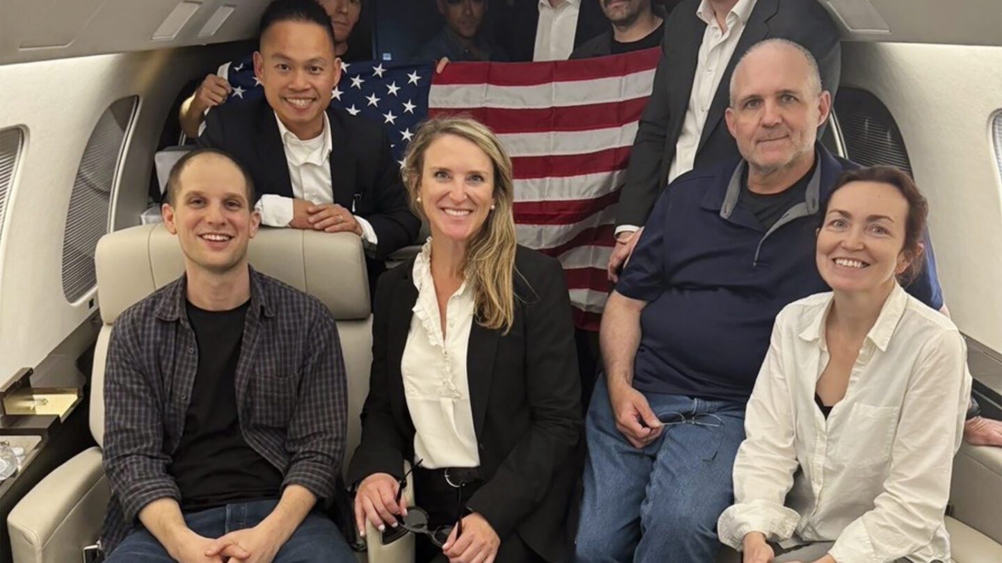 Evan Gershkovich, left, Alsu Kurmasheva, right, and Paul Whelan, second from right, and others pose for a picture aboard a plane, Thursday, Aug. 1, 2024, following their release from Russian captivity.