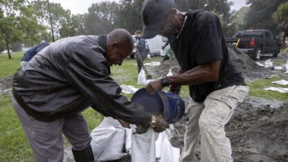 In the pouring rain, Hershey Stepherson, left, and Bryan Burc, right, use a five gallon bucket to fill a sandbag while preparing for Hurricane Debby, Monday, Aug. 5, 2024, in Savannah, Ga.