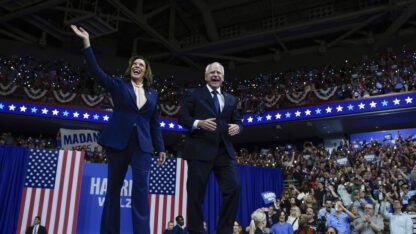 Democratic presidential nominee Vice President Kamala Harris and her running mate Minnesota Gov. Tim Walz attend a campaign rally in Philadelphia. Harris raises her hand in greeting to the rallygoers.