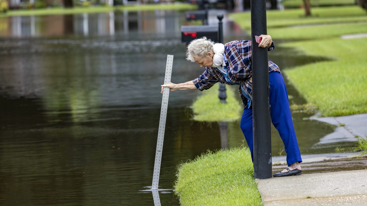 A resident measures the depth of the flooded street with storm water from Tropical Storm Debby.