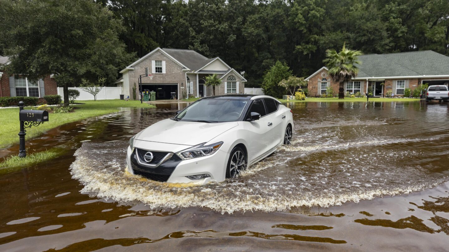 A car drives through water in a flooded neighborhood.