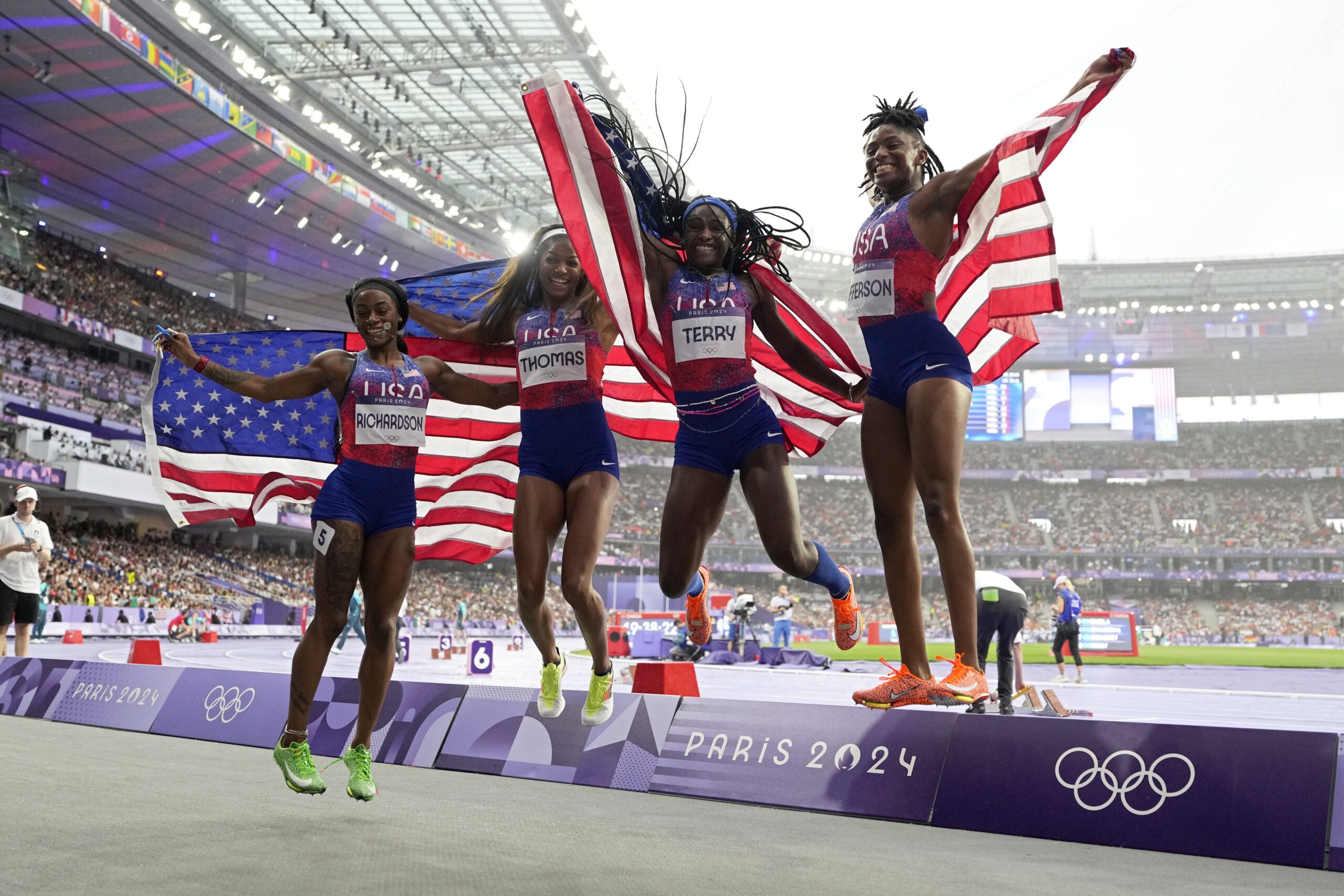 Sha'carri Richardson,Gabrielle Thomas, Twanisha Terry, and Melissa Jefferson, of the United States jump in unison, each holding American flags behind them.