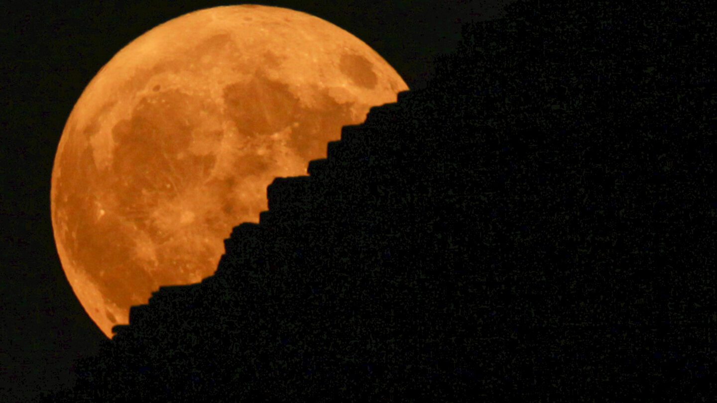 An orange supermoon rises behind the Giza Pyramids.