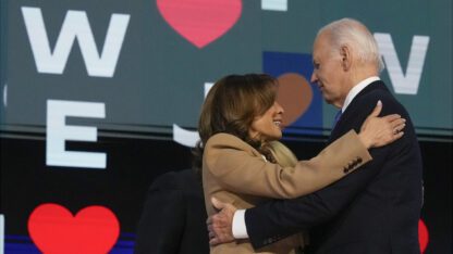 Joe Biden and Kamala Harris embrace in front of a backdrop at the Democratic National Convention.