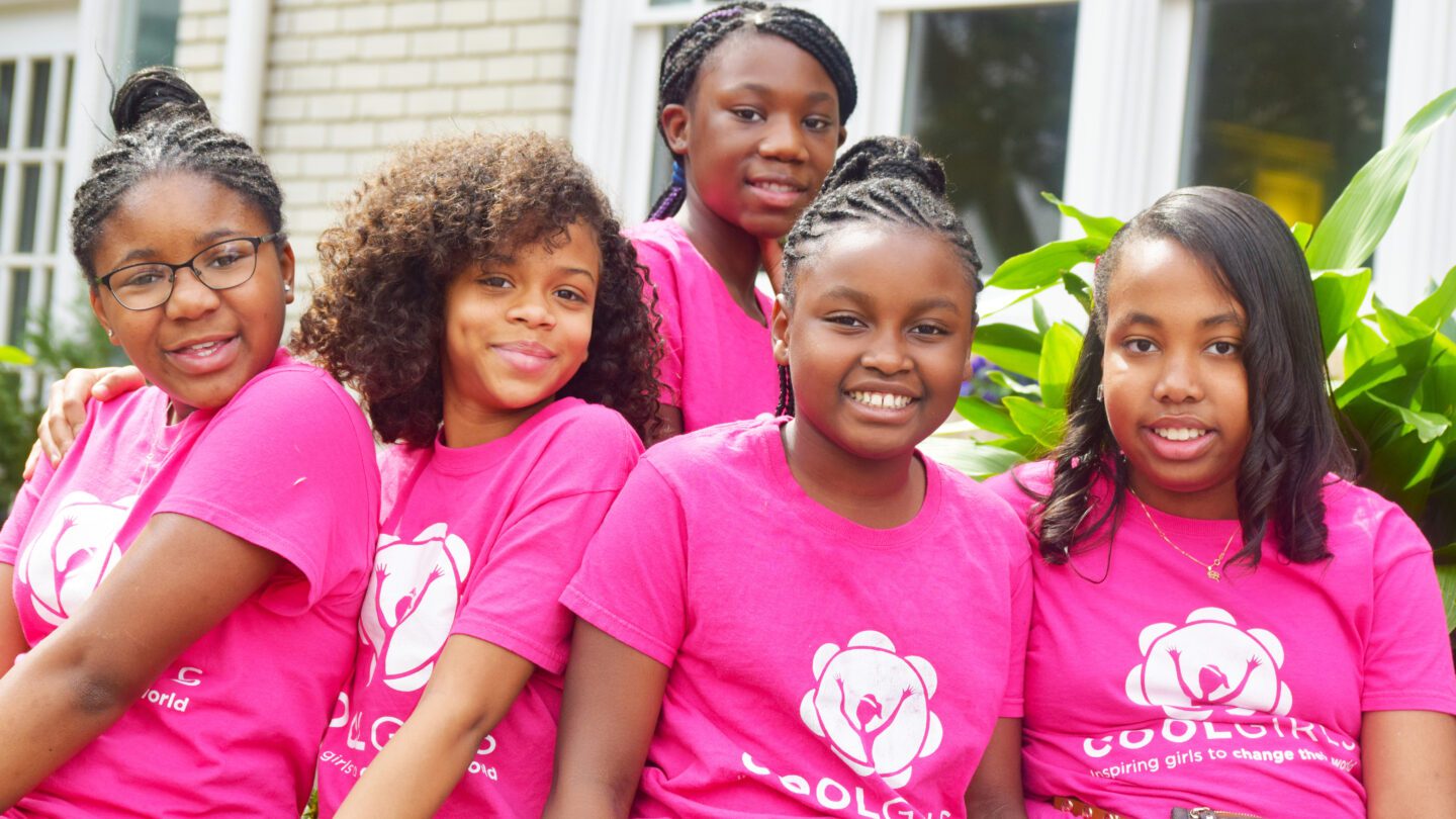 Several young girls wearing bright pink Cool Girls T-shirts pose for a photo.