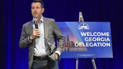 David Plouffe stands with a microphone at the Democratic National Convention in front of a sign that says Welcome Georgia Delegation.