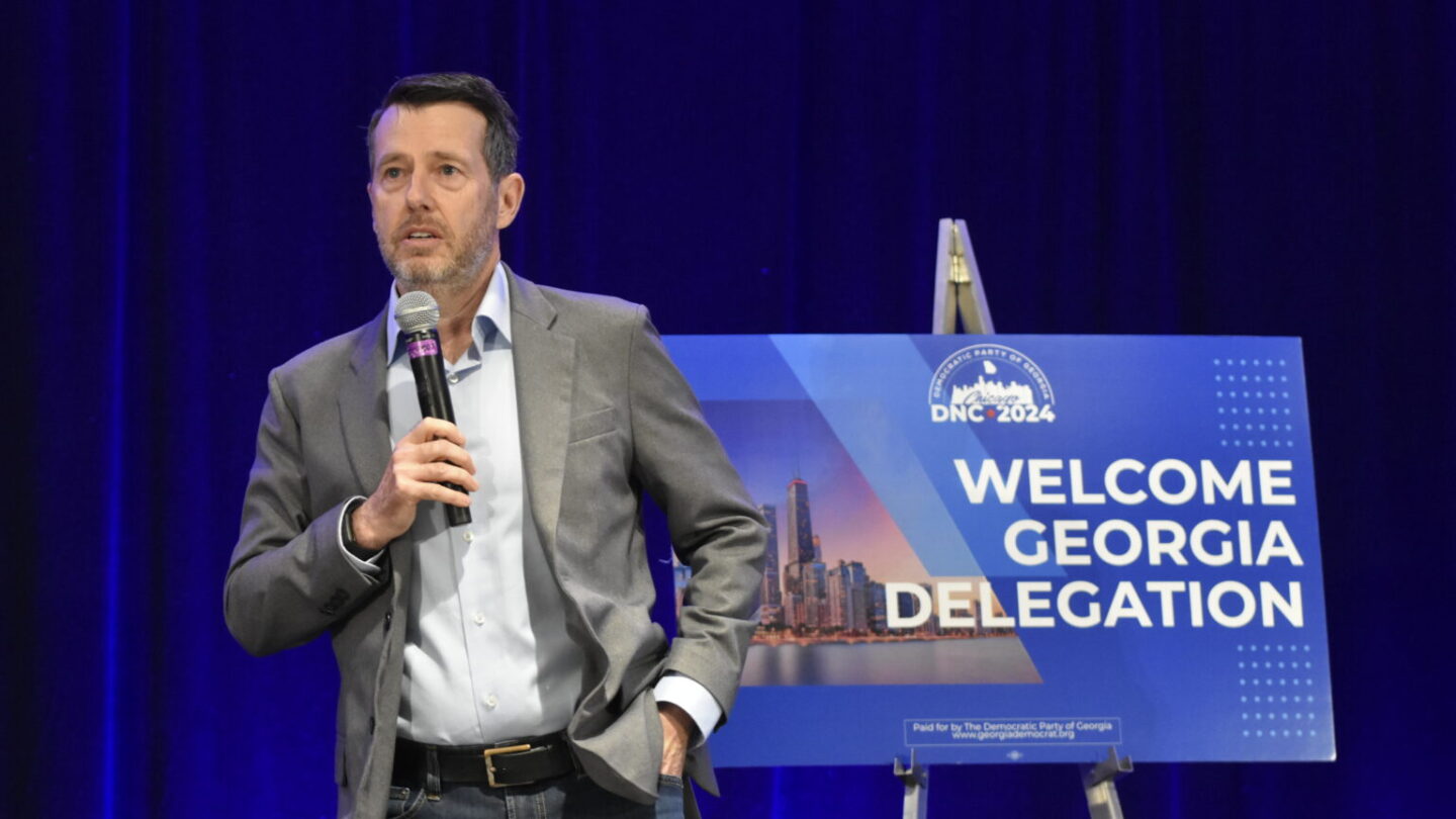 David Plouffe stands with a microphone at the Democratic National Convention in front of a sign that says Welcome Georgia Delegation.