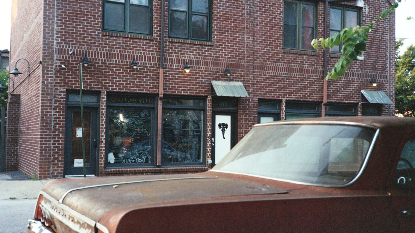 A brown car is parked outside of the brick wall of Ernies in the Cut barbershop.