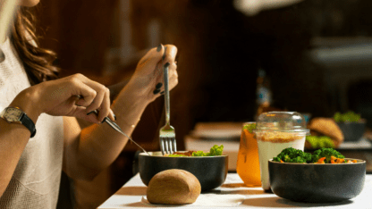 A pair of hands hold a fork and knife over a bowl of vegetables.