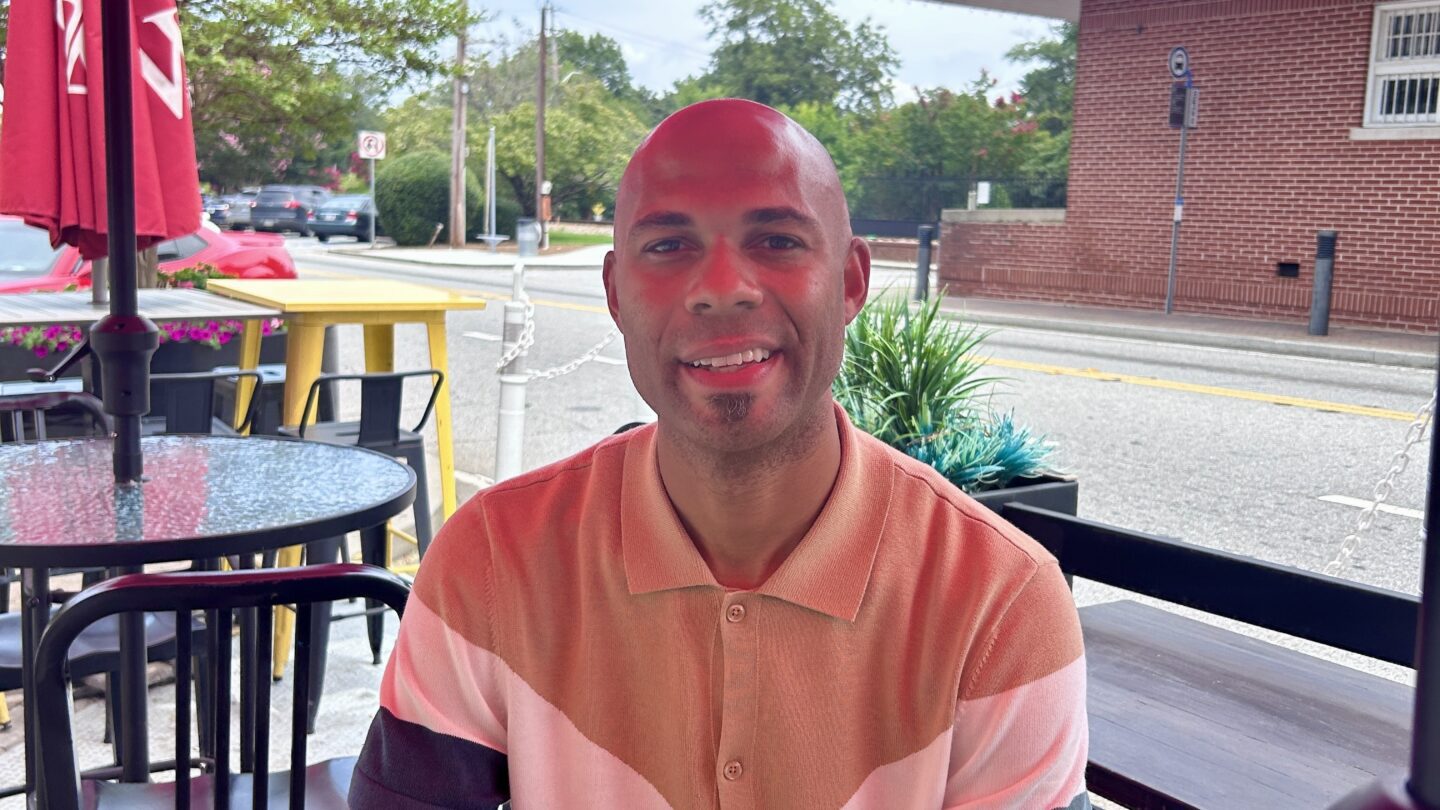 Warren Luckett sits at a patio table with a red shade.