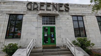 The front of he Greene's Fine Foods store, which has a green door with large lettering spelling out GREENES above it.