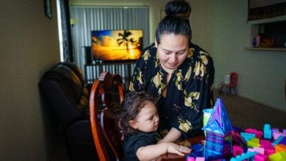 Annalinda Martinez holds her two-year-old son at the kitchen table of their apartment as they play with magnetic tiles and blocks.