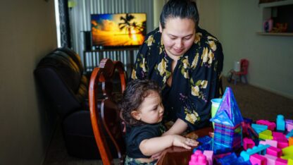 Annalinda Martinez holds her two-year-old son at the kitchen table of their apartment as they play with magnetic tiles and blocks.