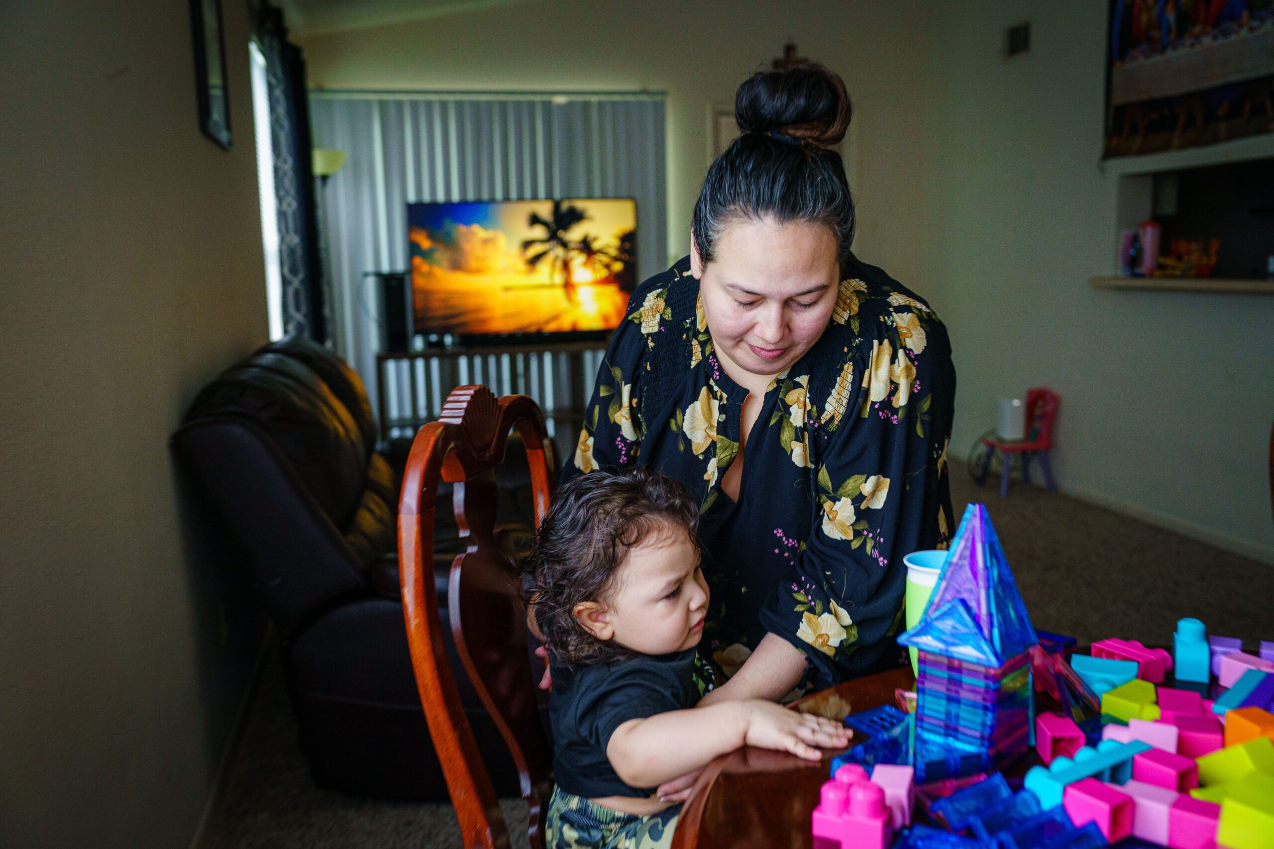 Annalinda Martinez holds her two-year-old son at the kitchen table of their apartment as they play with magnetic tiles and blocks.