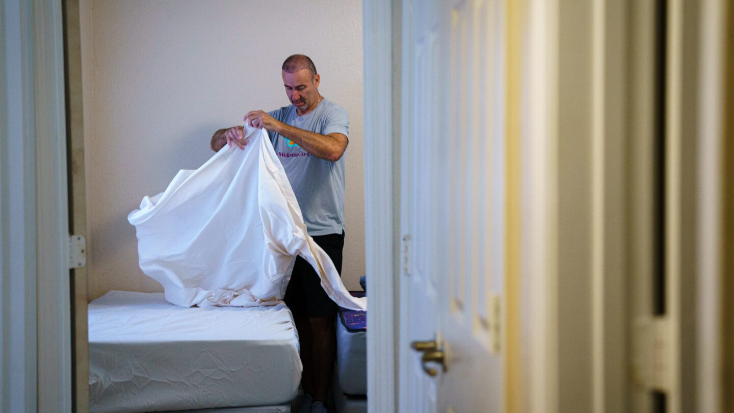 A man makes a bed in an apartment.