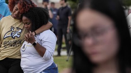 Two people embrace in the background as people attend a vigil for the school shooting in Apalachee High School.