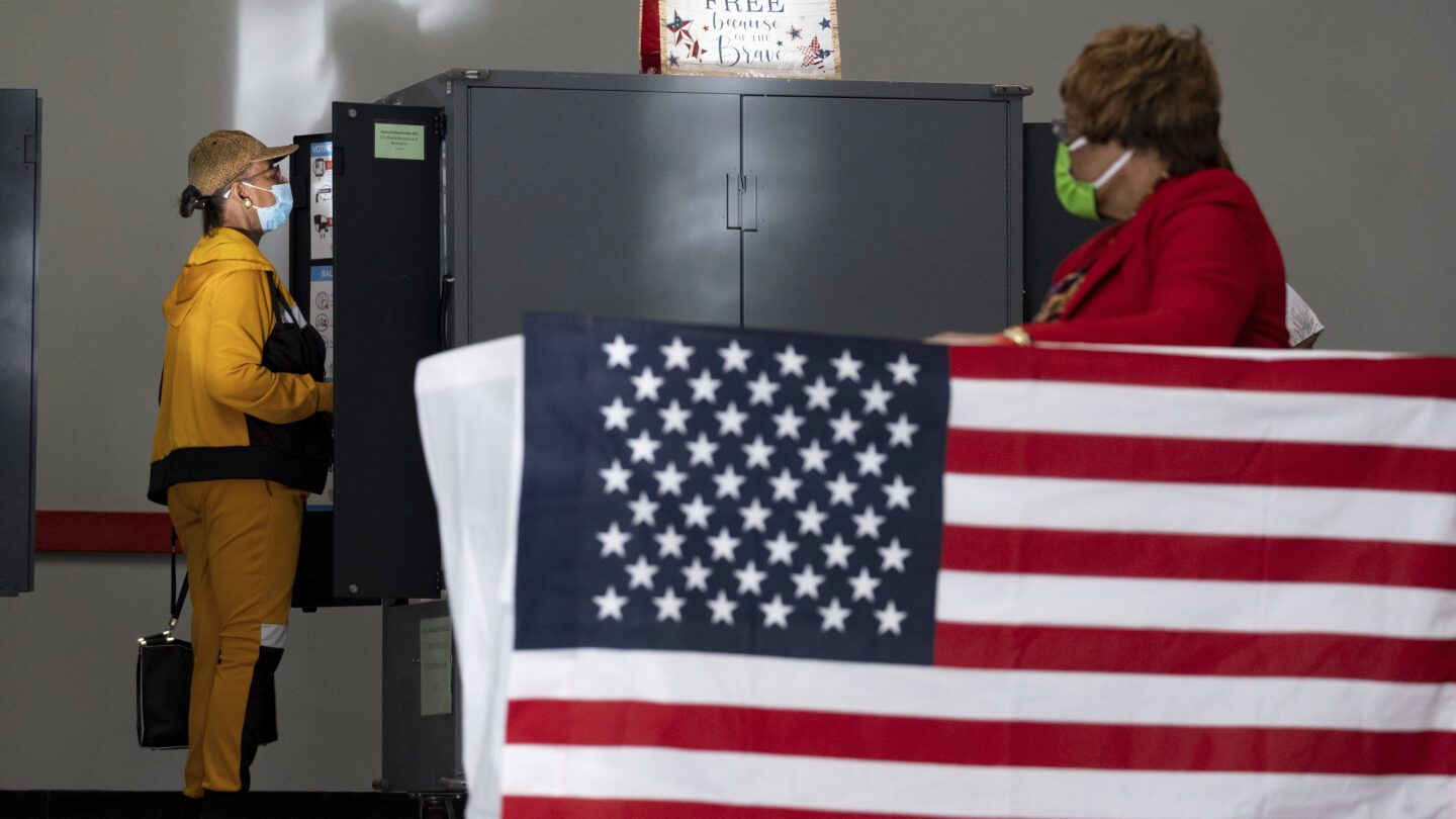 A voter marks her ballot during the first day of early voting in Atlanta, Oct. 17, 2022. A large American flag is next to the ballot boxes.