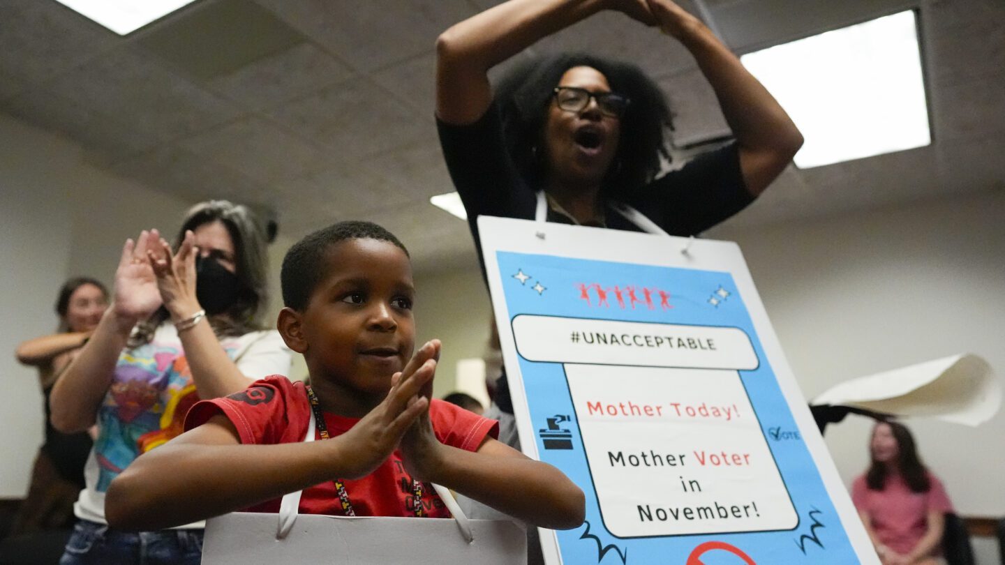 Parents and children raise their hands, carrying signs around their necks.