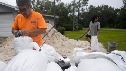 A man and his son fill sand bags on top of a mound of sand.