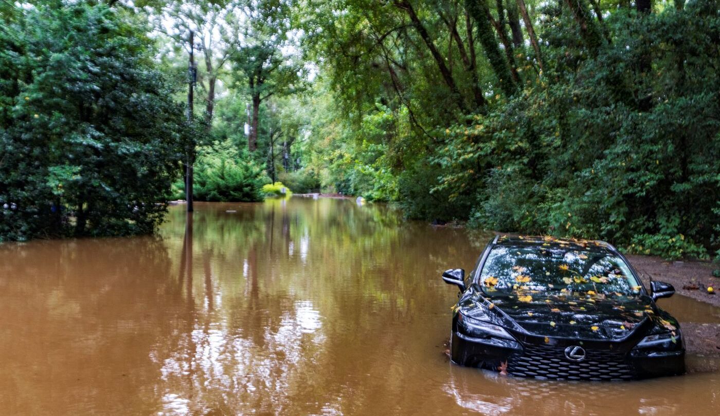 A partially submerged vehicle in a pool of brown water, surrounded by trees.