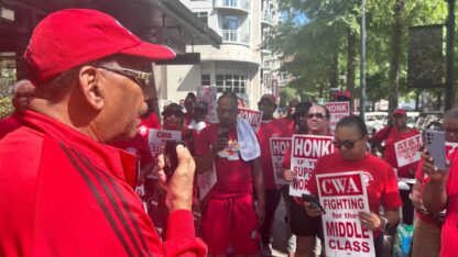 CWA President Claude Cummings Jr. speaks as striking workers listen. All wear red CWA shirts.