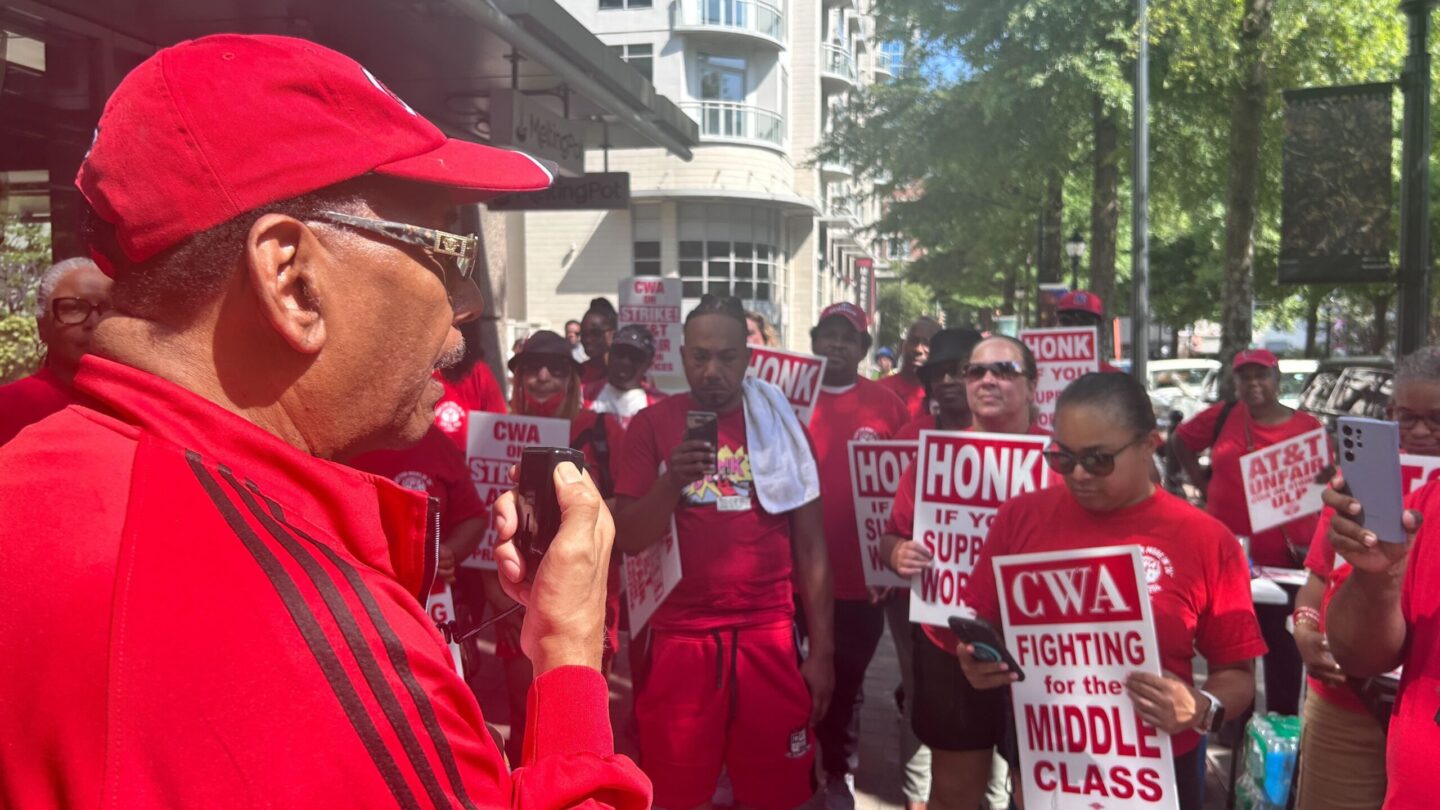 CWA President Claude Cummings Jr. speaks as striking workers listen. All wear red CWA shirts.