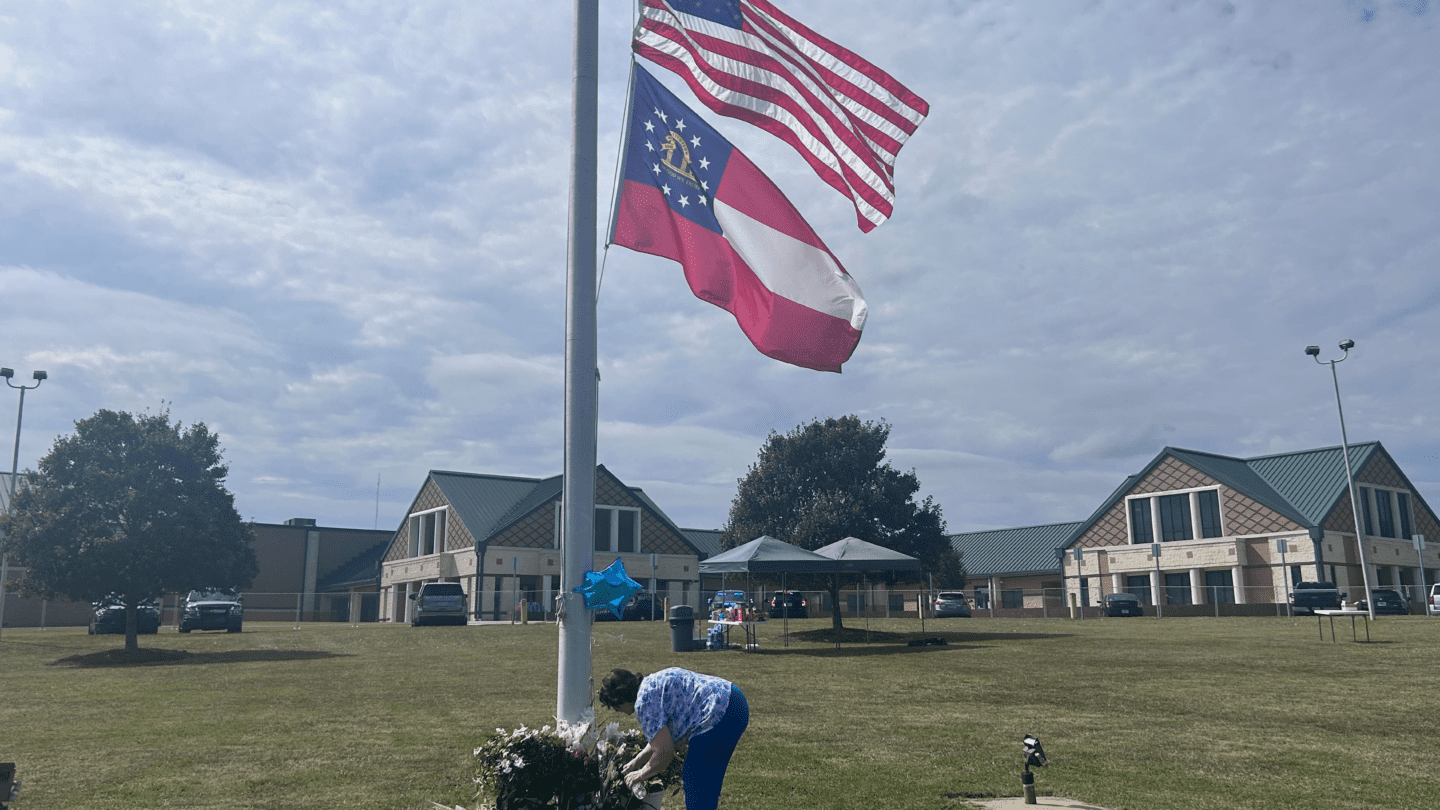 A person places flowers at the foot of a flag pole at half-mast.