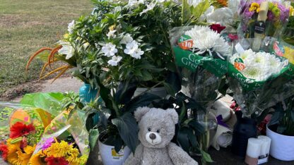 A bear and several bouquets of flowers surround a flag pole in a vigil to the victims of Apalachee High School in Winder, Georgia.