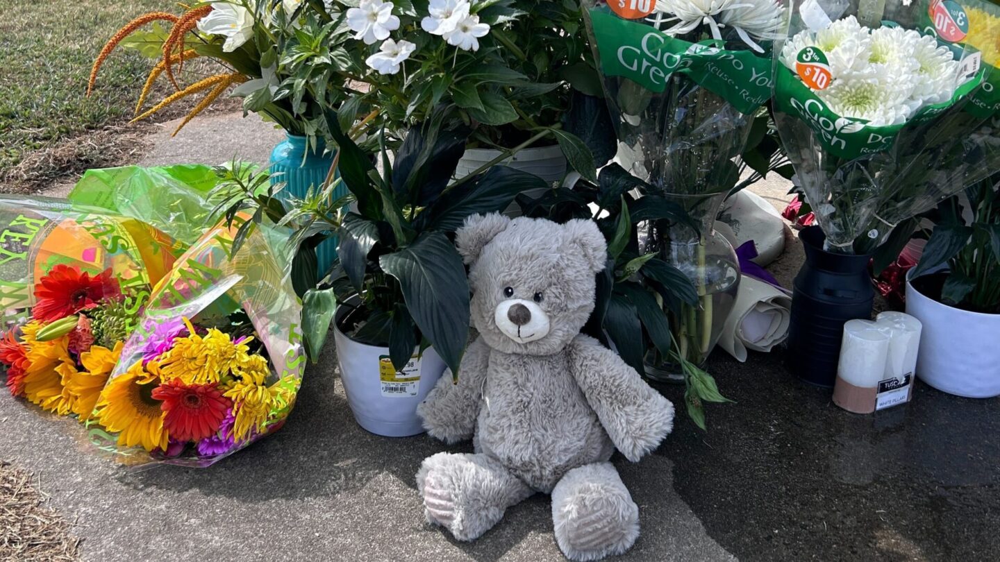 A bear and several bouquets of flowers surround a flag pole in a vigil to the victims of Apalachee High School in Winder, Georgia.