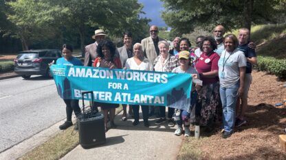 A group of people stand together and hold a blue sign that reads, Amazon Workers For a Better Atlanta.