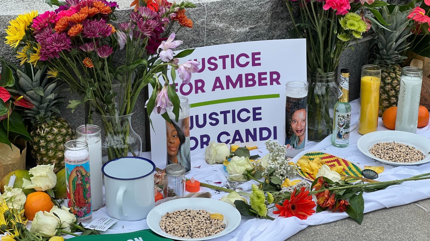 A vigil with flowers and a sign saying Justice for Amber and Justice for Candi with their pictures. Candles surround the vigil.