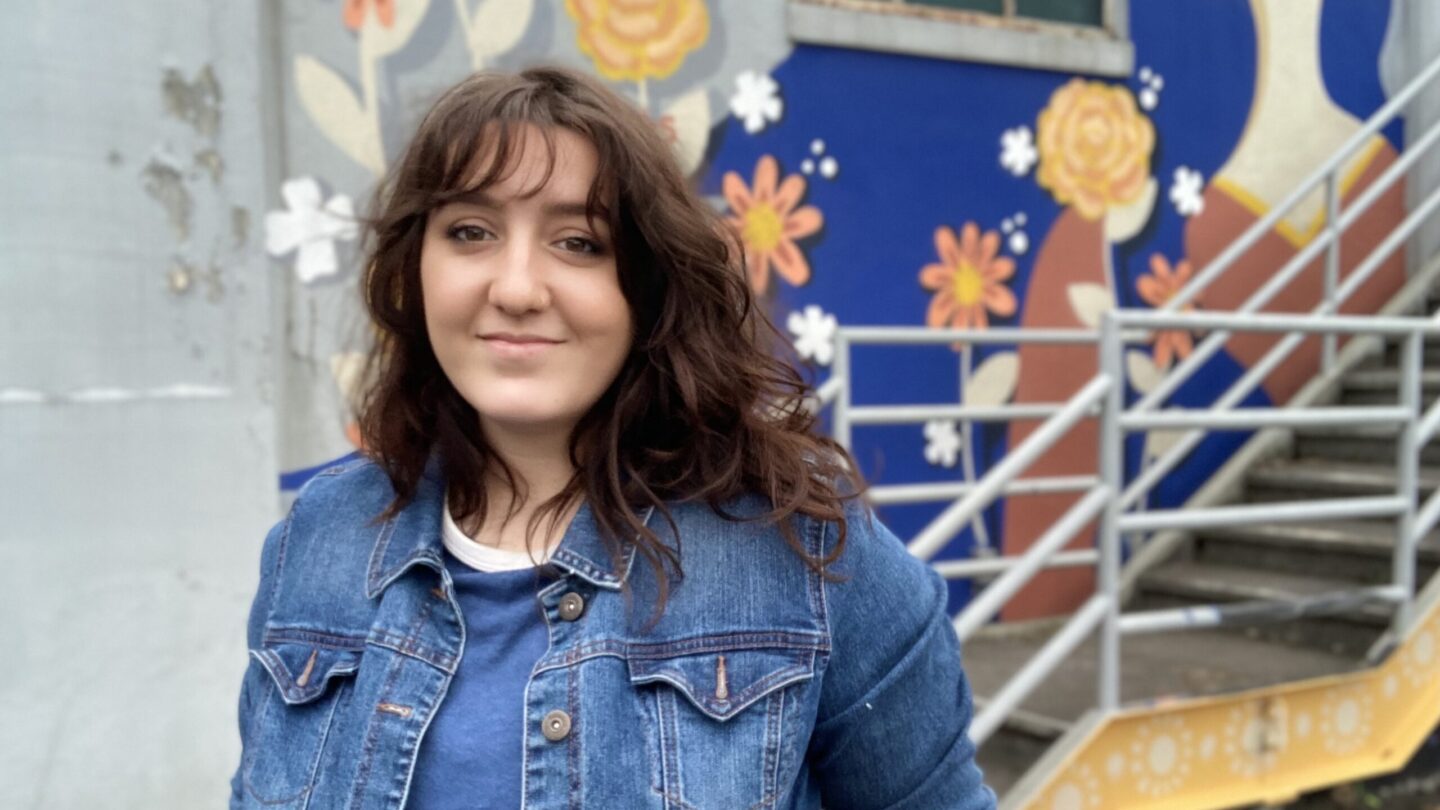 Nicole Merizalde poses in front of a blue and yellow mural behind a staircase.