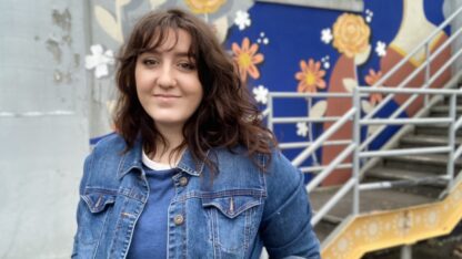 Nicole Merizalde poses in front of a blue and yellow mural behind a staircase.