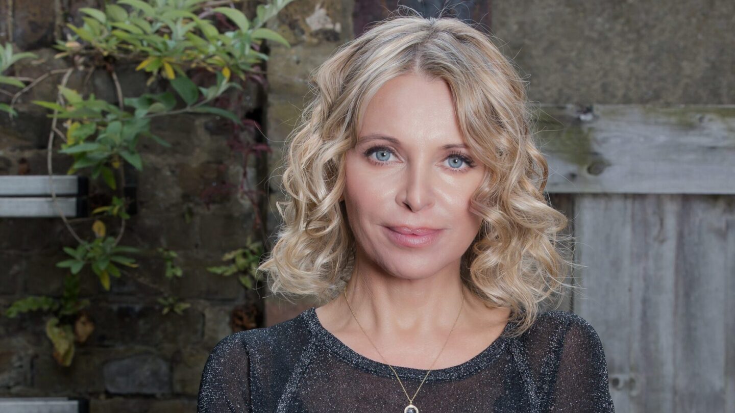 Nikki Bedi poses for a photograph against a wooden fence.