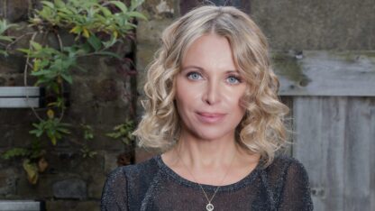 Nikki Bedi poses for a photograph against a wooden fence.