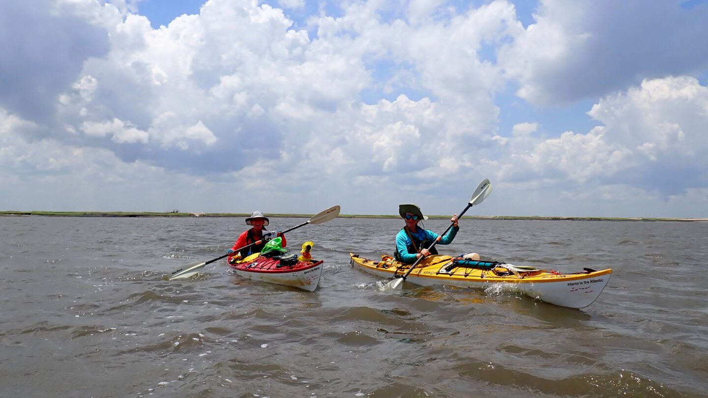 Two people in kayaks under a blue sky.