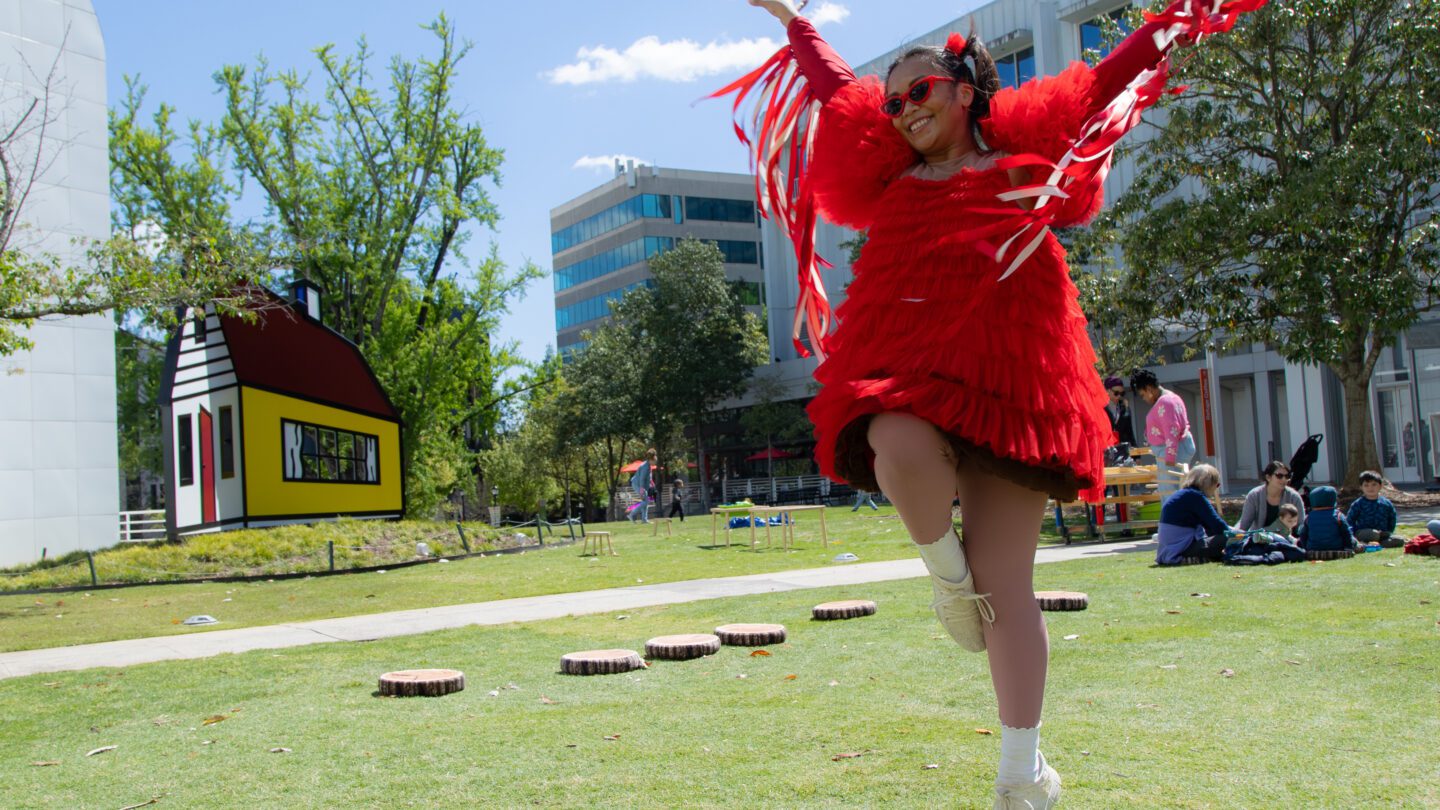 A person is running around in a backyard, wearing a shirt with red tassels and a red dress.