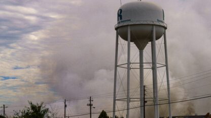 A plume of smoke in the air behind a water tower.